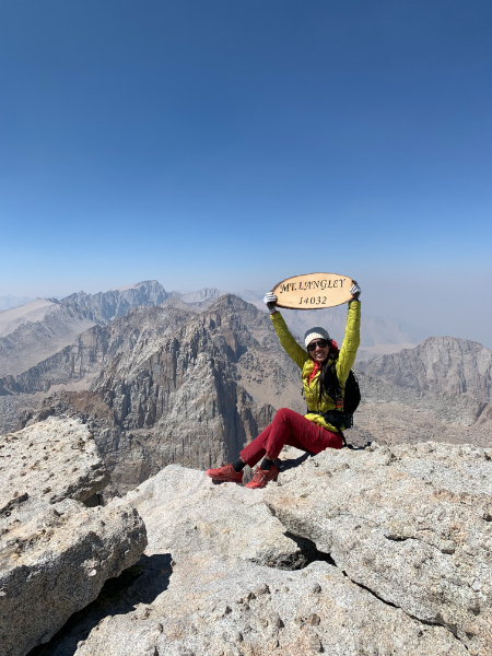 girl in yellow and red holding mt langley sign with whitney in the back