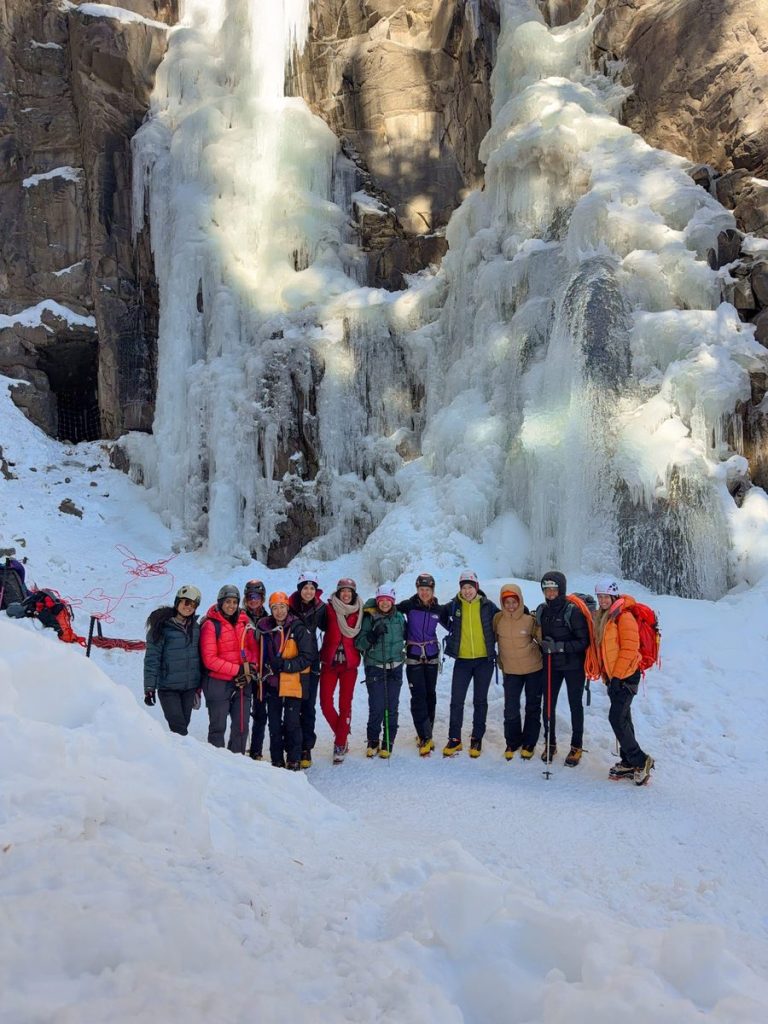 The 2026 women’s retreat group beneath sunlit frozen waterfalls in Ouray